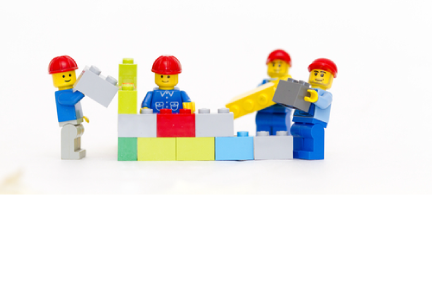 Lego people using the Lego blocks to build a wall. 